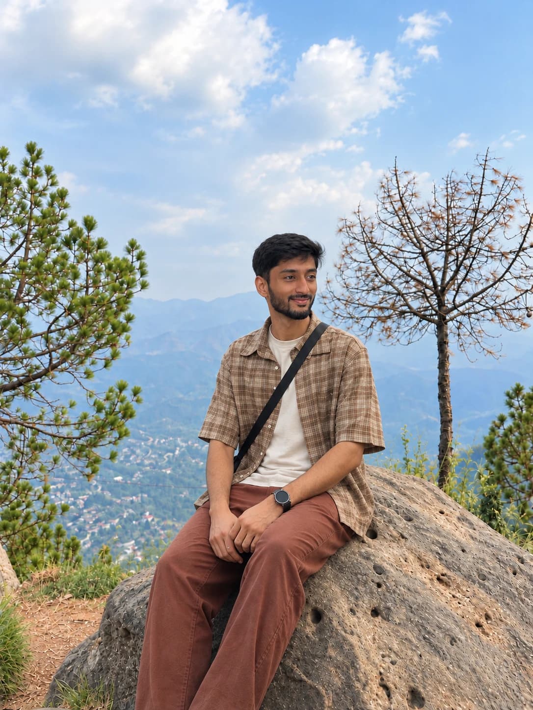 Aashir sitting on a rock above a green valley, smiling and looking off to the side